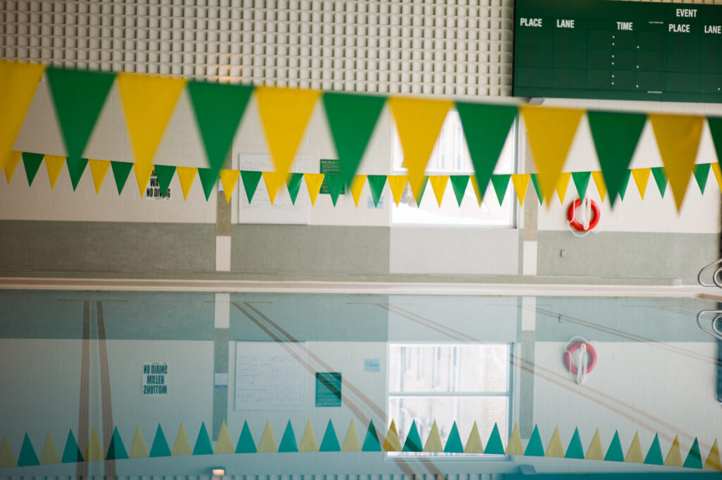 An indoor pool with green and gold flags hanging above it.