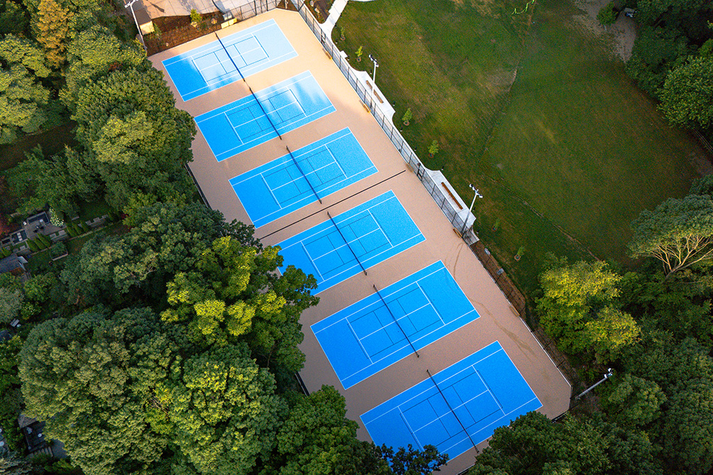 Aerial view of six tennis courts with a blue surface.